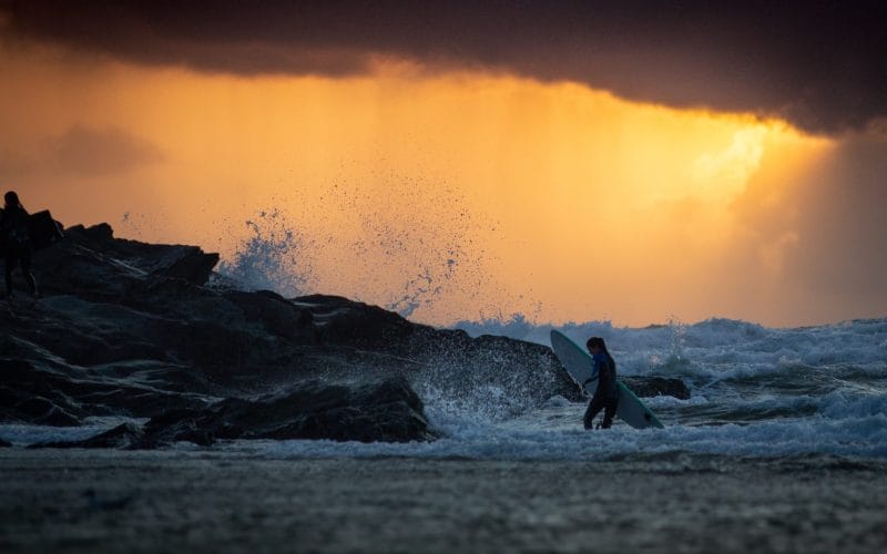 Person carrying surfboard in sea at newquay.