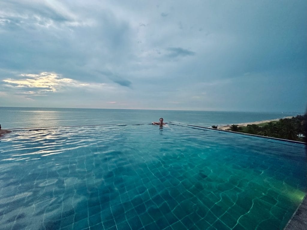 Man in rooftop infinity pool overlooking negombo beach.